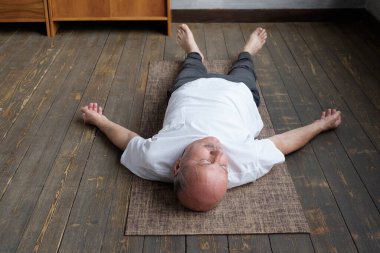 Yoga. Kıdemli adam ahşap bir zeminde meditasyon yapıyor ve Shavasana pozunda yatıyor..