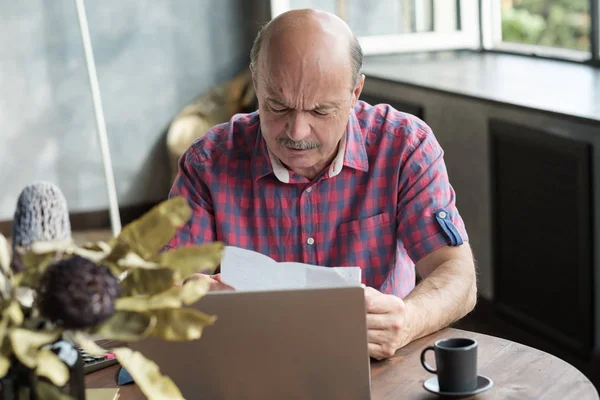 Старший лысый мужчина оплачивает счета своим ноутбуком — стоковое фото