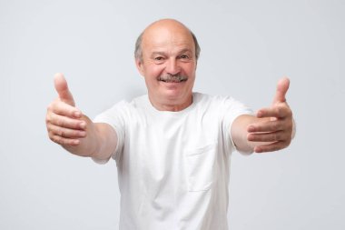 Senior man pulling hands towards camera, wanting to cuddle, smiling broadly