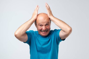 Terrifed troubled senior keeps hands on head, being shocked hearing bad news