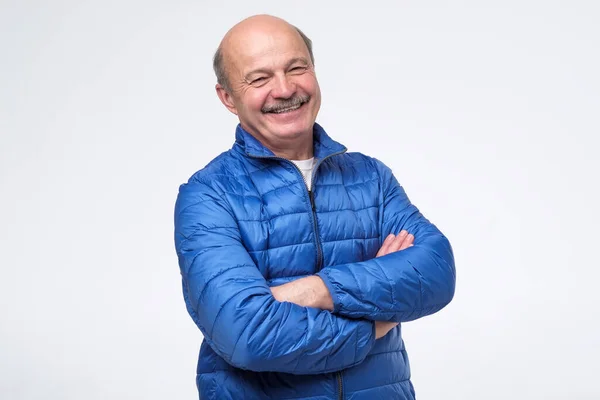 Homem sênior de casaco azul com braços cruzados sorrindo — Fotografia de Stock