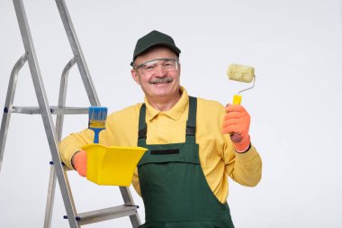 Painter senior man at work with a paint roller, standing near ladder.