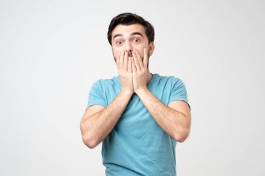 Beyaz İspanyol bir adam, eli ağzında, sersemlemiş ve nutku tutulmuş, beyaz arka planda soyutlanmış. Stüdyo çekimi