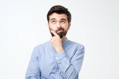 İspanyol bir adamın yukarı bakıp, beyaz arka planda çenesini ovuşturduğunu düşünüyor. Takma uzaya bakan genç ve düşünceli bir işadamı.