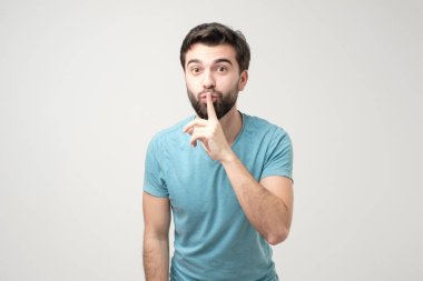 Ciddi yakışıklı bir adam parmaklarını dudaklarının üzerinde tutar, komployu sürdürmeye çalışır. Sessiz olun lütfen..