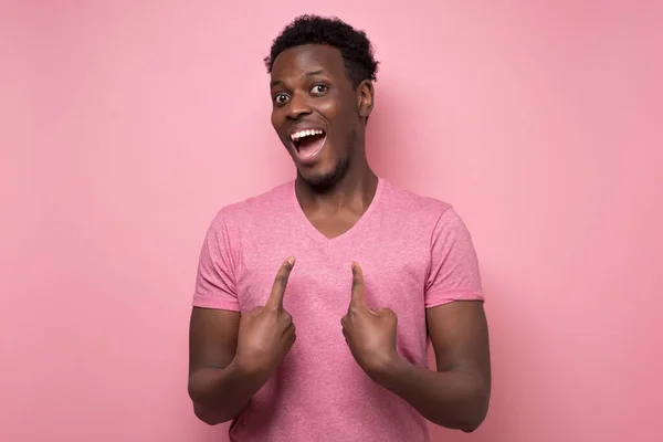 Joven africano positivo sonriendo y señalándose a sí mismo con los dedos índice . — Foto de Stock