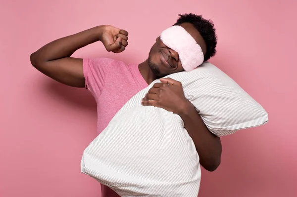 Africano americano negro hombre durmiendo abrazando un almohada usando dormir máscara . — Foto de Stock