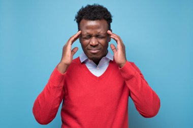 Stüdyoda başı ağrıyan kırmızı kazaklı ciddi bir Afro Amerikalı.