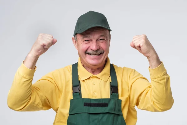 Trabajador senior, hombre con gorra verde y ropa excitado sosteniendo puños . — Foto de Stock