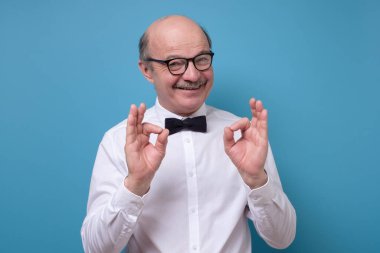 Beyaz tişörtlü beyaz adam kameraya gülümsüyor. Mavi duvarda pozitif yüz insani duyguları