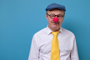 Hüzünlü, üzgün, palyaço burnu takmış, mavi arka planda ağlayan adam.