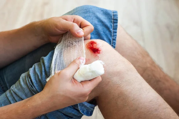 Man heals the wound on his knee at home. Holding the bandage at the hands