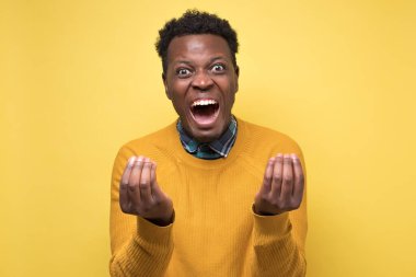 Yakışıklı Afrikalı kızgın görünüyor sarı arka planda İtalyan jesti gösteriyor. Adam sinirlenmiş. Negatif yüz insani duygularının stüdyo çekimi.