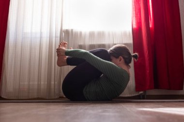 Gülümseyen çekici kadın yerde yoga yapıyor, diz çöküp göğüs egzersizi yapıyor, Apanasana evde oturma odasında poz veriyor.