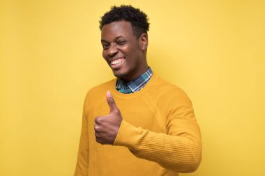 Sarı duvarda baş parmağını gösteren neşeli tavırlı yakışıklı siyahi adam. Seçimini onayla. Olumlu yüz insani duygu