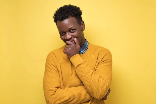 Joven hombre afroamericano en suéter amarillo contemplando un plan escondiendo sonrisa . — Foto de Stock