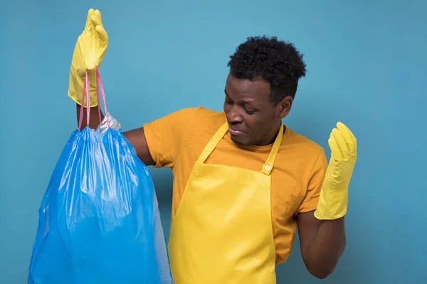 Африканский американец в фартуке и перчатках держит вонючий мешок для мусора — стоковое фото
