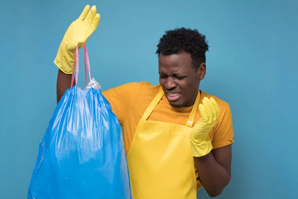 Hombre afroamericano en delantal y guantes sosteniendo una bolsa de basura apestosa — Foto de Stock