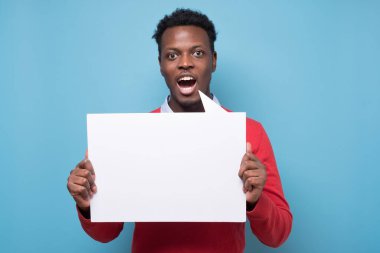Stüdyonun mavi arka planında boş beyaz tabela tutan Afrikalı Amerikalı bir adam.