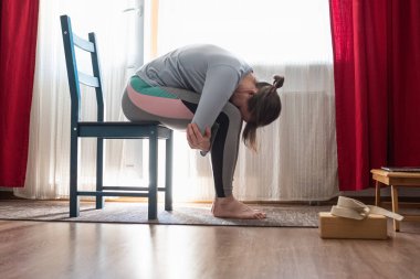 Rahatlatıcı yoga pozu veren genç bir kadın. Adı Balasana veya çocuk pozu. Sandalyede oturuyor.