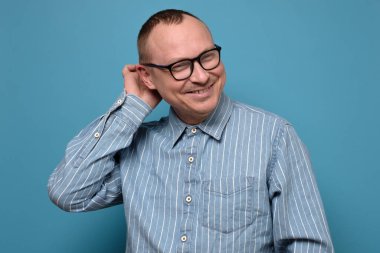 Olgun bir adam utangaç ve gururlu görünüyor. Mavi arka planda iltifatlarla gururlanıyor. İnsanlar, insani duygular ve ifadeler. Vücut dili.