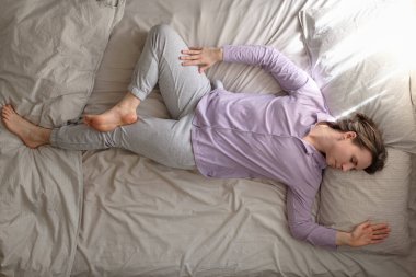 Genç, beyaz bir kadın yatakta çalışıyor. Spinal Twist yapıyor. Jathara Parivartanasana, sabah antrenmanından sonra dinleniyor.