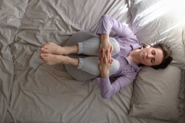 Genç bir kadın evde çalışıyor, yatakta omurga için yoga egzersizi yapıyor, diz çöküp göğüse poz veriyor, sabahları Pawanmuktasana 'da gaz çıkarma pozisyonu alıyor. Üst görünüm