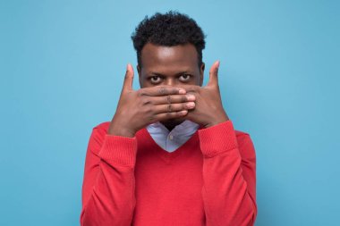 Çekici Afrikalı genç bir adam avuçlarını kapatıp neler olduğunu görmek için röntgencilik yapıyor. Stüdyo resmi mavi duvarda.