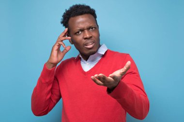 Pensive young african man against a blue background. What are you speaking about concept. Studio shot clipart