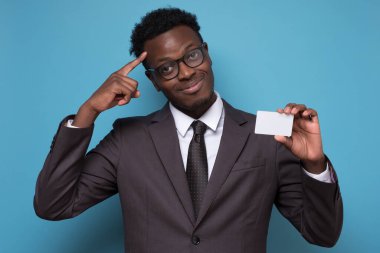 Takım elbiseli genç Afro-Amerikan adam elinde boş kredi kartı üreten bir fikir tutuyor. Stüdyo resmi mavi duvarda.