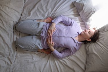 Sabahları yatakta uzanan kahraman yoga pozu veren beyaz bir kadın. Üst görünüm