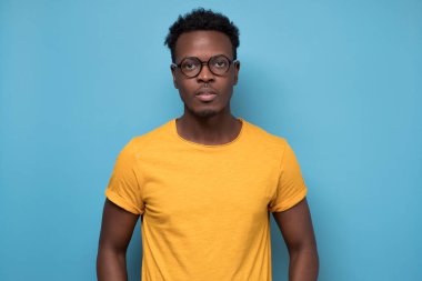 Gözlüklü akıllı Afro-Amerikan adam mavi arka plandaki kameraya bakıyor.