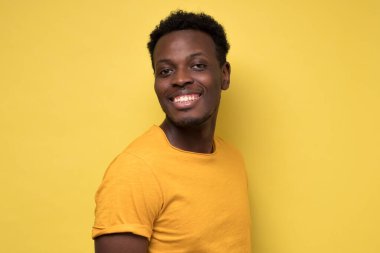 Sarı arka planda kameranın önünde poz veren sıradan bir Afrikalı genç..