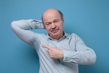 Hiperhidroz ya da sıcak hava nedeniyle terli tişörtlü yaşlı İspanyol bir adam. Stüdyo resmi mavi duvarda.