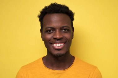 Sarı arka planda kameranın önünde poz veren sıradan bir Afrikalı genç. Görüntüyü kapat.