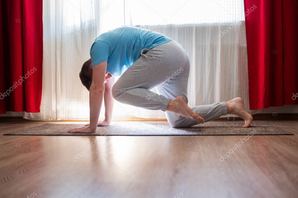 Young caucasian man practices yoga asana chakravakasana or bird pose at the living room at home.