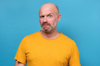 Kuşkulu sakallı, beyaz, güvensiz, olgun bir adam haberlere ya da hükümete inanmıyor. Mavi duvarda negatif insani duygular.