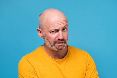 Kuşkulu sakallı, beyaz, güvensiz, olgun bir adam haberlere ya da hükümete inanmıyor. Mavi duvarda negatif insani duygular.