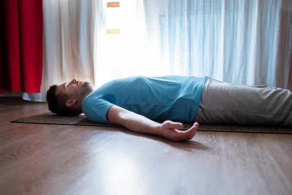 Jovem meditando em um chão e deitado em Shavasana posar em sua sala de estar . — Fotografia de Stock