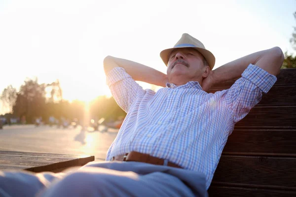 Älterer hispanischer Mann mit Sommermütze sitzt draußen auf Bank. — Stockfoto