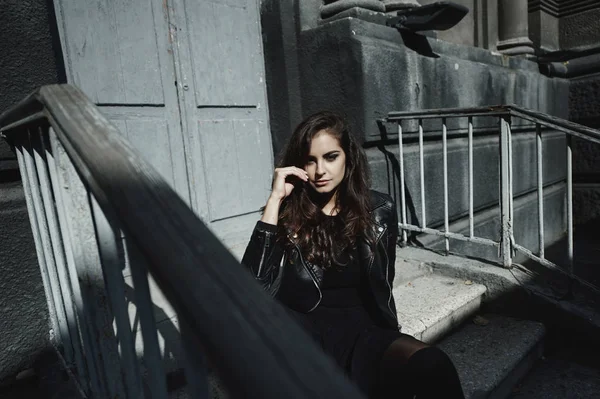 Eastern beautiful woman wearing biker jacket poses in backyard of vintage apartment house — Stock Photo, Image