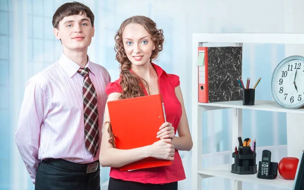 Young and smiling employees of the company, a man and a woman posing in the office workplace.