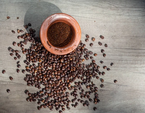 Black coffee ground in a clay mortar and in grains on the surface of a wooden table in sunny rays, with place for text. Top view.