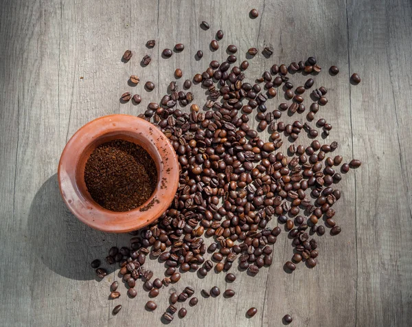 Black coffee ground in a clay mortar and in grains on the surface of a wooden table in sunny rays. Top view.