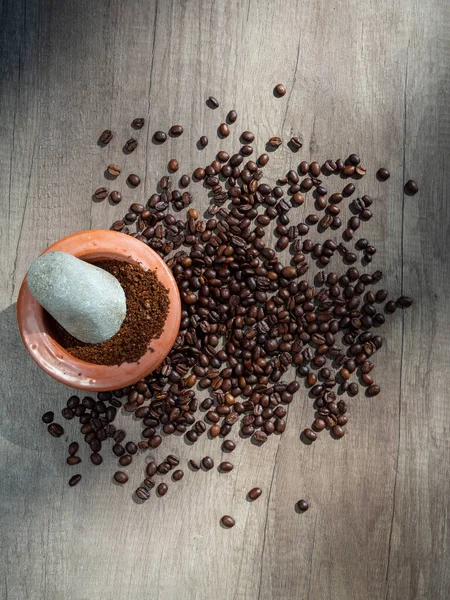 Black coffee ground in a clay mortar and in grains on the surface of a wooden table in sunny rays, with place for text. Top view.