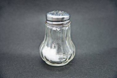 Salt shaker made of glass against a black background clipart