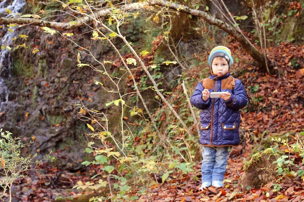 Niño pequeño de pie en el bosque al aire libre con teléfono móvil — Foto de Stock