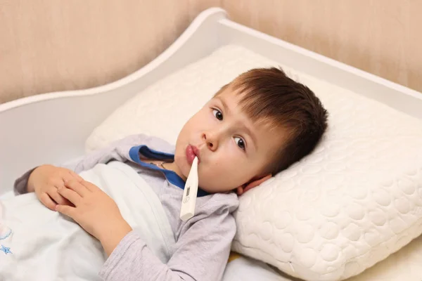 Niño enfermo acostado en la cama con un termómetro — Foto de Stock