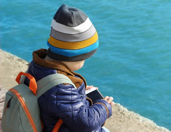 Lindo bebé niño con un teléfono celular en un banco al aire libre en el — Foto de Stock