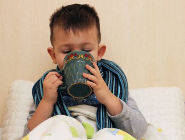 Bir bardak çay, tıp gribi tutan bir fularlı küçük hasta çocuk 